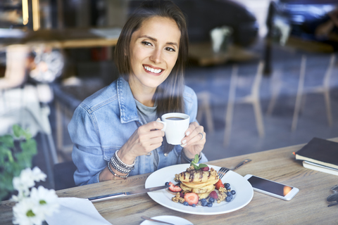 Portrait of smiling young woman enjoying pancakes and coffee in cafe stock photo