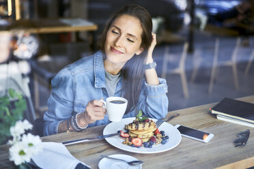 Smiling young woman enjoying pancakes and coffee in cafe - BSZF00580