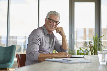 Portrait of smiling mature man using laptop on table at home - RBF06498