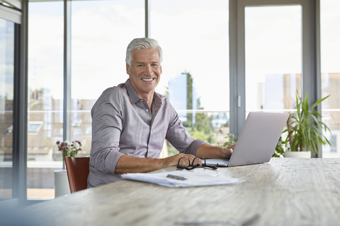 Portrait of smiling mature man using laptop on table at home stock photo