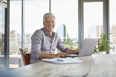 Portrait of smiling mature man using laptop on table at home - RBF06503