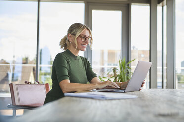 Lächelnde reife Frau mit Laptop auf dem Tisch zu Hause - RBF06508