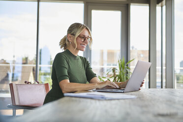 Smiling mature woman using laptop on table at home - RBF06508