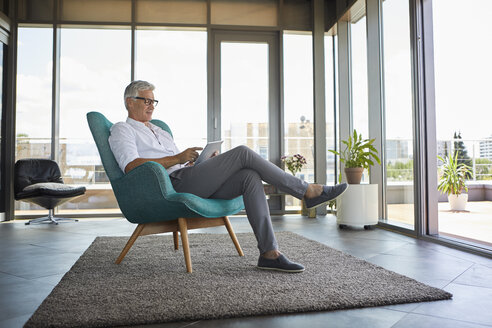 Mature man sitting in armchair at home using tablet - RBF06514