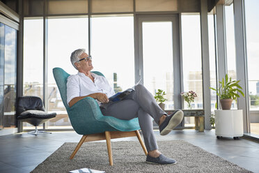 Mature man with a brochure relaxing in armchair at the window at home - RBF06519