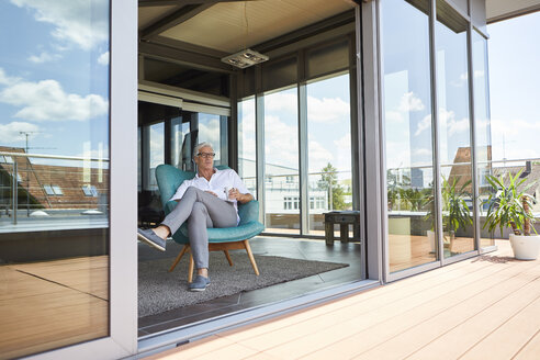 Älterer Mann entspannt sich im Sessel auf der Dachterrasse zu Hause - RBF06524