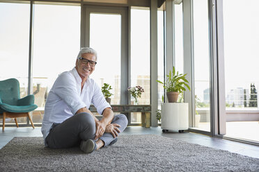 Smiling mature man relaxing sitting on carpet at home - RBF06526