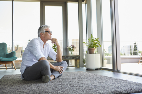 Pensive mature man sitting on carpet at home stock photo