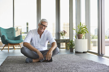 Porträt eines lächelnden reifen Mannes, der zu Hause auf einem Teppich sitzt - RBF06533