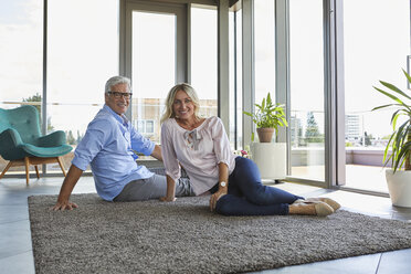 Porträt eines lächelnden reifen Paares, das sich zu Hause auf einem Teppich sitzt - RBF06558