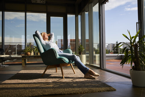 Mature woman relaxing in armchair in sunlight at home - RBF06564