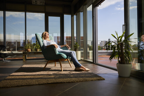 Reife Frau entspannt im Sessel im Sonnenlicht zu Hause - RBF06565