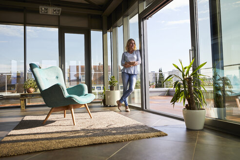 Mature woman standing at the window at home looking out - RBF06567