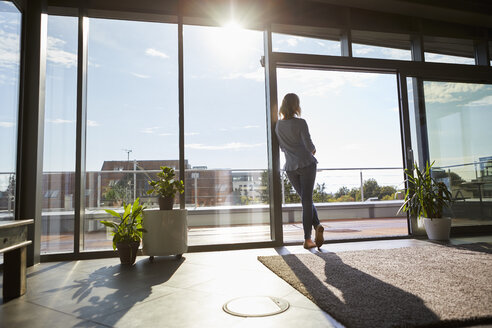 Back view woman in backlight standing at the window at home looking out - RBF06569