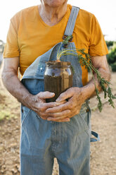 Senior man holding glass jar with soil and growing carrot - JRFF01836