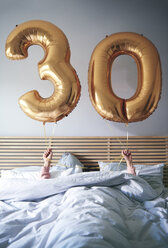 Frau mit goldenen Luftballons, die ihren Geburtstag im Bett feiert - ABIF00963