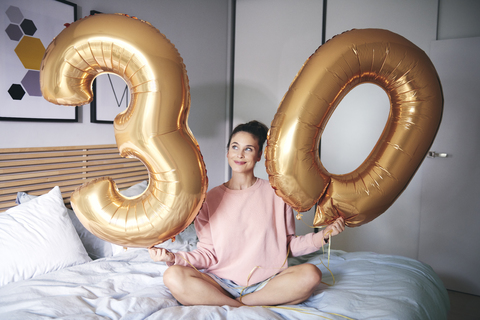 Glückliche Frau hält goldene Luftballons am Geburtstagsmorgen, lizenzfreies Stockfoto