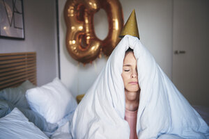 Traurige Frau, die ihren Geburtstag feiert und unter einer Decke auf dem Bett sitzt - ABIF00982