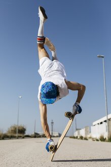 Rückenansicht eines Mannes in stilvollem, sportlichem Outfit, der auf einem Skateboard steht, kopfüber vor blauem Himmel - JRFF01852