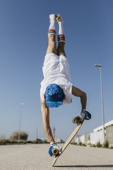 Rückenansicht eines Mannes in stilvollem, sportlichem Outfit, der auf einem Skateboard steht, kopfüber vor blauem Himmel - JRFF01853