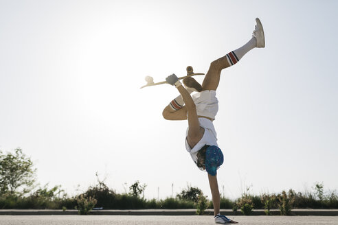 Side view of sportive man doing exciting trick with skateboard flipping on one hand on street - JRFF01855