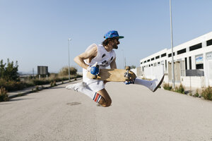 Sportlicher Mann springt mit Skateboard auf Händen über den Boden - JRFF01859