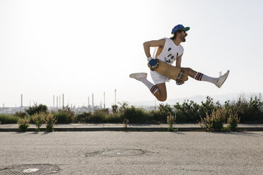 Sportlicher Mann springt mit Skateboard auf Händen über den Boden - JRFF01860