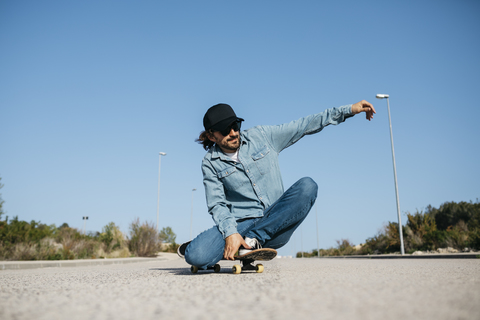 Trendiger Mann in Jeans und Mütze beim Skateboarden, lizenzfreies Stockfoto