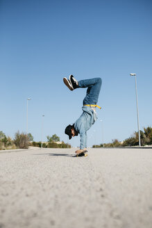 Trendiger Mann in Jeans und Mütze beim Skateboardfahren, stehend auf dem Skateboard kopfüber - JRFF01864