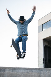 Trendy man in denim and cap skateboarding, doing jump with skateboard from concrete ramp - JRFF01865