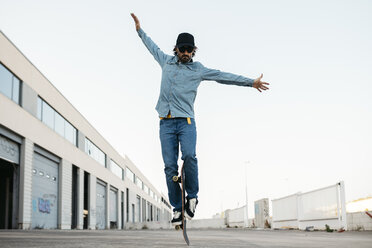 Trendy man in denim and cap skateboarding, standing on skateboard - JRFF01868