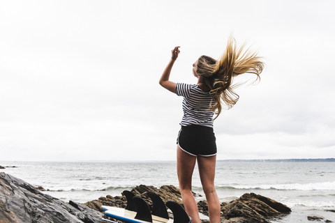 Junge Frau mit Surfbrett tanzt am Strand, lizenzfreies Stockfoto