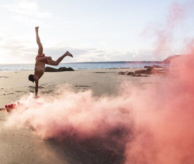 Man doing movement training at the beach with red smoke - UUF15053