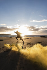 Mann beim Bewegungstraining am Strand mit buntem Rauch bei Sonnenuntergang - UUF15055