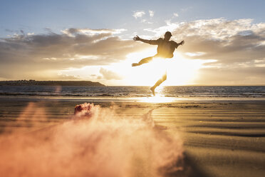 Man doing movement training at the beach with colorful smoke at sunset - UUF15062