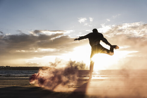 Man doing movement training at the beach with colorful smoke at sunset - UUF15065