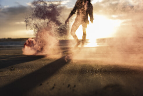 Young man running on the beach at sunset with colorful smoke - UUF15066