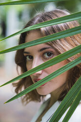 Young woman looking through palm leaf, portrait - KKAF01665