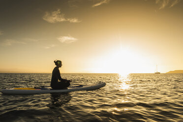 Young woman meditationg on paddleboard at sunset - UUF15068