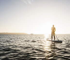 Junge Frau Stand Up Paddle Surfing bei Sonnenuntergang - UUF15074