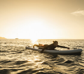 Junge Frau auf Paddleboard bei Sonnenuntergang liegend - UUF15075