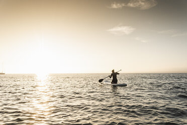 Young woman stand up paddle surfing at sunset - UUF15076