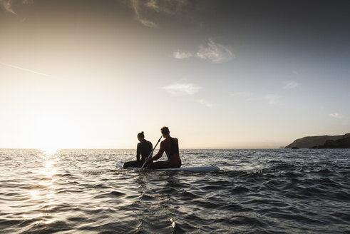 Paar beim Paddeln auf dem Paddleboard bei Sonnenuntergang auf dem Meer - UUF15078