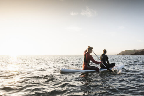 Paar beim Paddeln auf dem Paddleboard bei Sonnenuntergang auf dem Meer - UUF15079