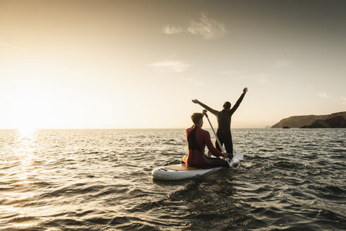 Paar beim Paddeln auf dem Paddleboard bei Sonnenuntergang auf dem Meer - UUF15080