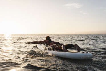 Junger Mann auf Paddleboard bei Sonnenuntergang - UUF15083