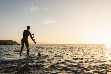 Junger Mann auf Paddleboard bei Sonnenuntergang - UUF15084