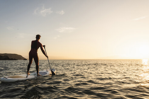 Junger Mann auf Paddleboard bei Sonnenuntergang - UUF15084