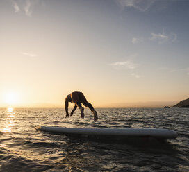 Junger Mann auf Paddleboard bei Sonnenuntergang - UUF15087
