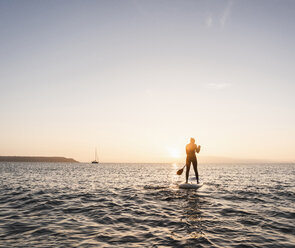 Young woman stand up paddle surfing at sunset - UUF15092